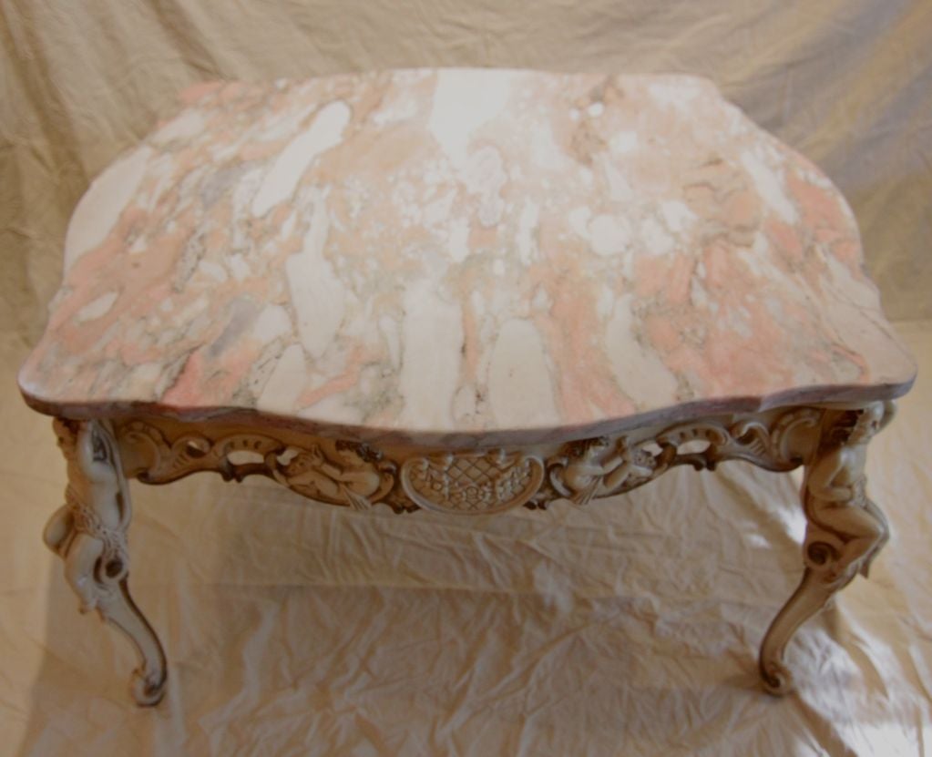 Large expansive coffee table Wood carved ornate base cherubs. pink gray marble top.<br />
34.5
