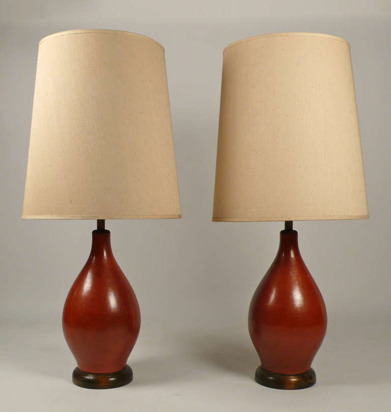 A pair of vintage modernist ceramic table lamps in a matte, oxblood colored glaze that resembles antique leather. Original parchment colored shades are included upon buyers request. Wood bases and fittings have a distressed finish. Price is for the