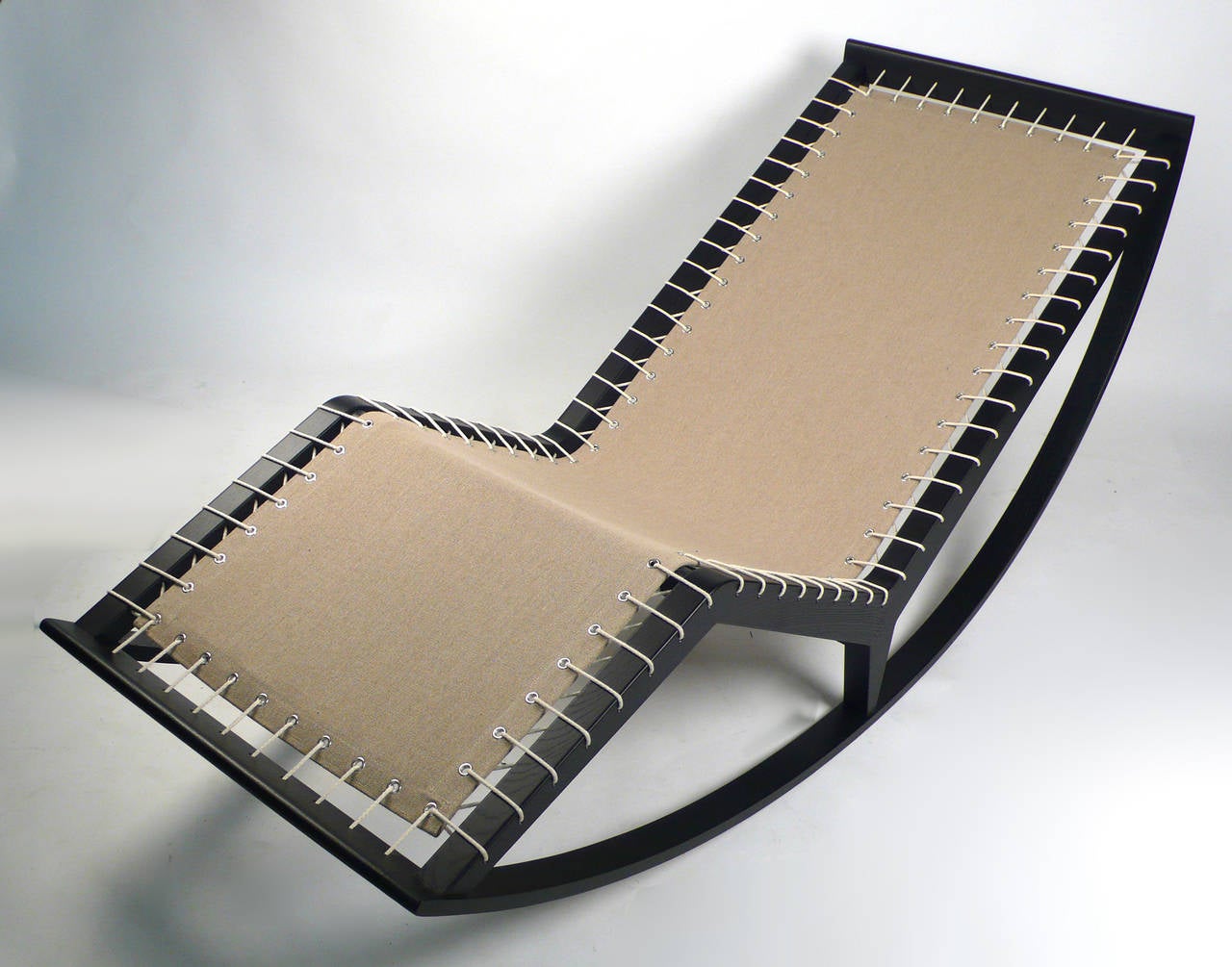 Wippende Chaiselongue mit Stützrahmen. Der Trägerstoff in Ecru ist mit Kordeln befestigt:: die an den Seiten ein grafisches Motiv ergeben. Die mit Stoff bezogene Polyurethan-Polsterung ist in Module unterteilt und kann über sich selbst gefaltet