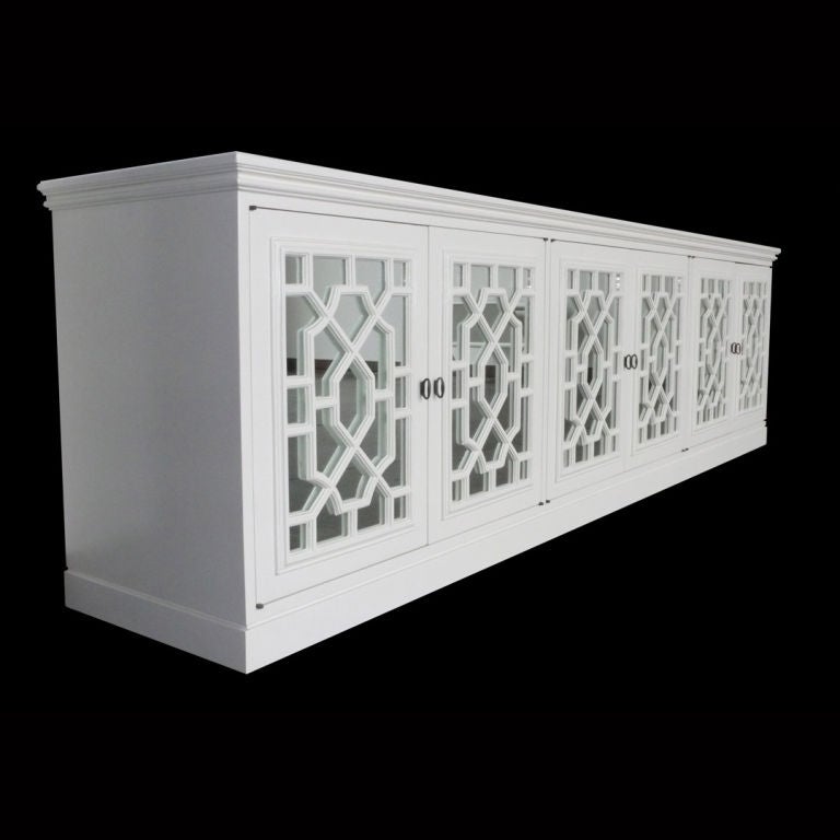Monumentally scaled 1960's Hollywood Regency Credenza. Restored in a french polished white lacquer. The chinese style fretwork is backed with mirrors. All three sets of doors open to reveal an adjustable shelf. A very substantial piece of cabinetry