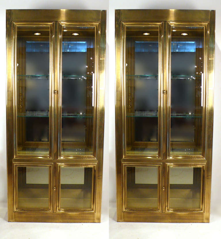 Pair of aged brass lighted vitrines by Mastercraft. Nice detailing.  This pair was hand selected by Jonathan Adler for the private shopping area of the short lived Barney's NY store at Northpark Center, Dallas, TX. 

Price is for the pair