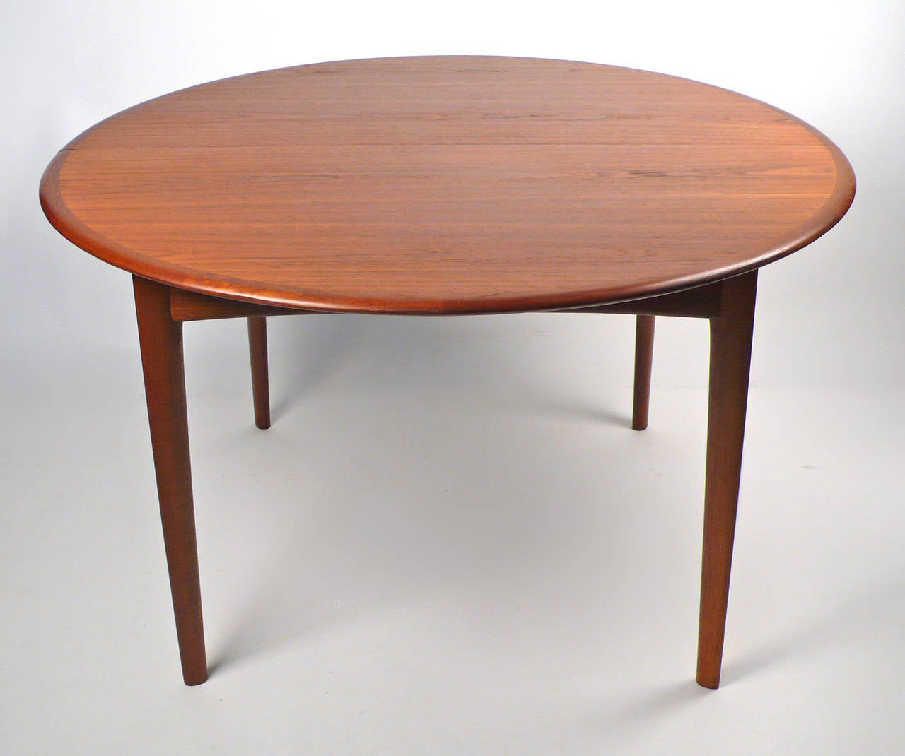 This Svend Madsen Danish modern dining table has a beautiful teakwood grain and four elegant solid wood tapering oval legs. Includes two leaves. Each leaf measures 24
