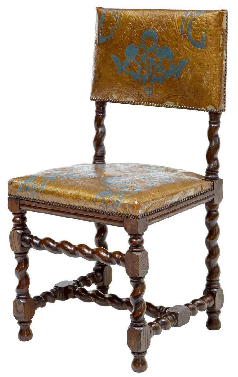 Here we have a very rare set of 18 Cromwellian-style dining chairs circa 1890.

These being covered in polychromed blue and gold painted leather, depicting an embossed floral, eagle and heraldic design.

Turned oak barley twist legs and