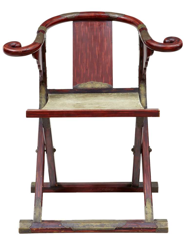 Good quality Mongol design folding armchair with horse shoe shaped back.

Featuring engraved brass mounts to the arm, back legs and feet, finished in a distressed red lacquer. Leather seat with legs folding in a scissor action.
