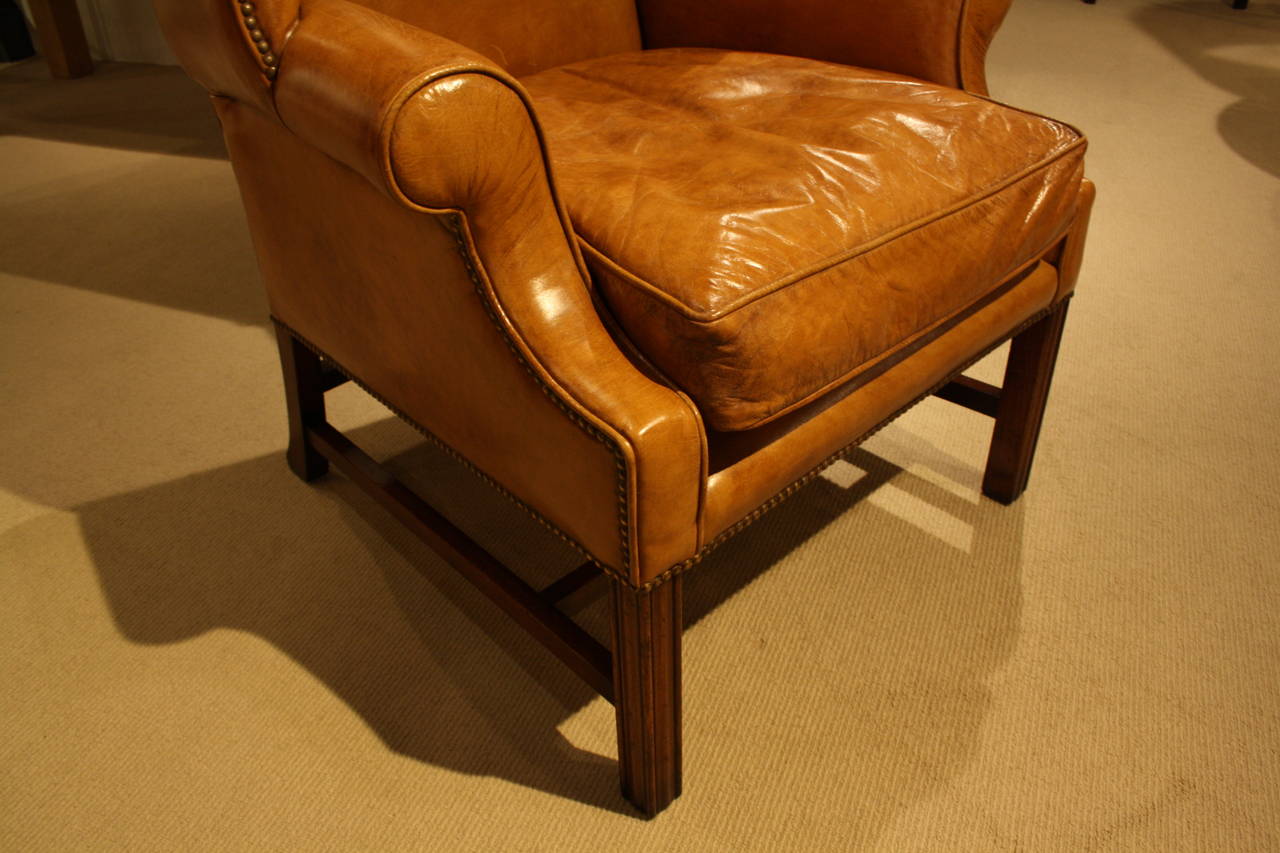 Sudbury wing chair in light tan leather with nailhead detailing and carved wooden legs.
