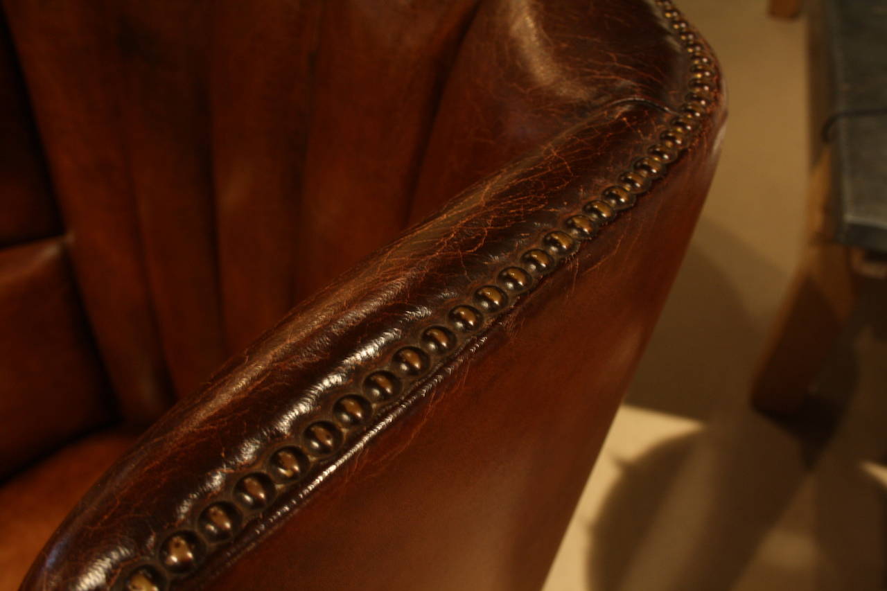 Selkirk wing chair in dark tan leather with a distressed finish. This chair features nailhead detailing with carved legs and casters.