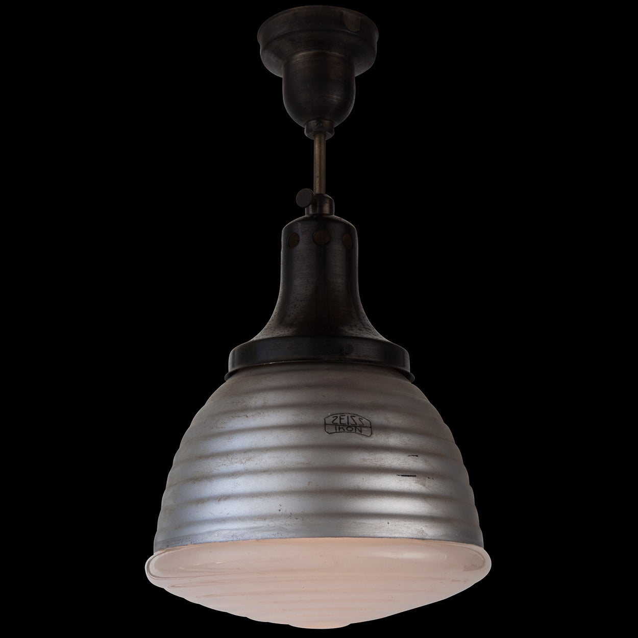 Industrial pendant with brass canopy and rod. The shade is ribbed silver painted metal with an opaline glass cap. 

The light socket is affixed to an adjustable rod that manipulates the light concentration. 

Designed by Adolf Meyer for Zeiss