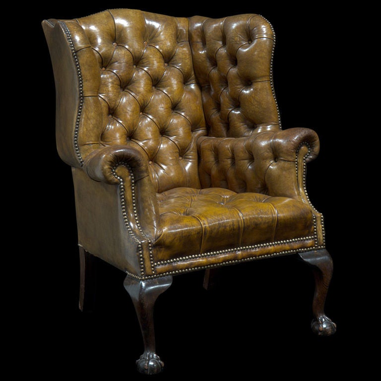 Monumental wingback leather library chair with original worn fabric, buttoned and tufted back and arms.