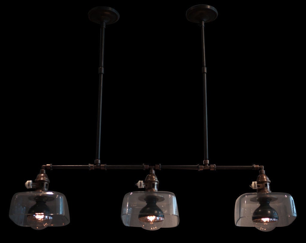 Industrial ceiling fixture with three square glass shades, connected with piping and fittings.