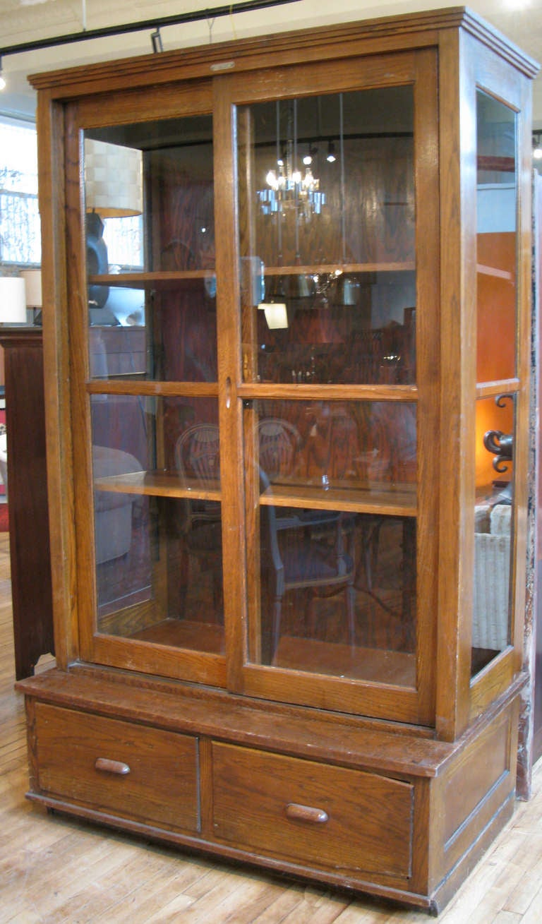 a very handsome antique 1930's oak display cabinet with glass panels on the sides and fitted sliding glass doors on the front. the display top mounts on a storage base with 2 large sliding drawers.