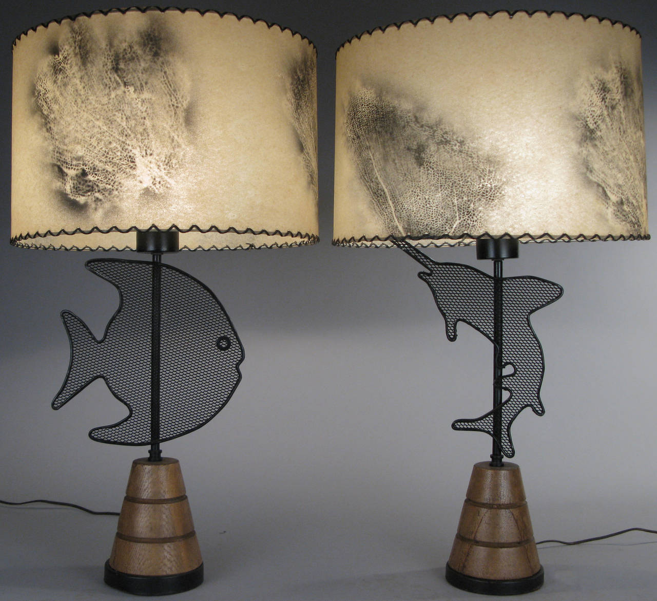 a pair of modern 1950's whimsical table lamps in the manner of Frederick Weinberg, with stacked wood bases, and wire mesh fish decoration on each lamp, together with their original parchment shades with fan coral markings.