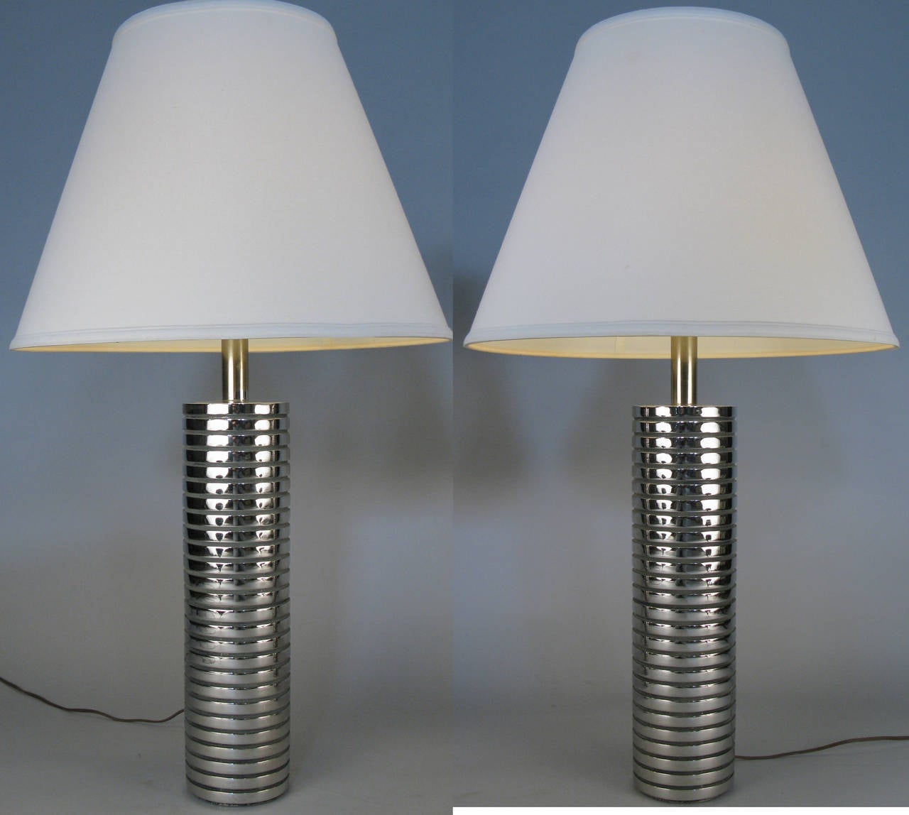 A very stylish pair of vintage 1950s table lamps with heavy bases of chromed steel ribbed cylinders, with their original white shades.