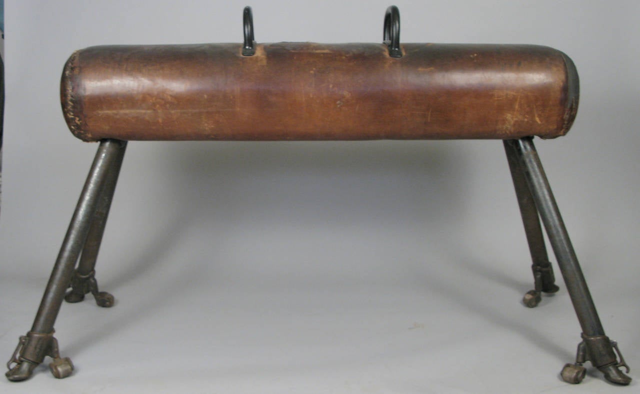 An antique 1920s gymnastics pommel horse with cast iron legs with their original retractable rollers, and a leather covered horse with replaced handles. Leather is worn but largely intact.

Dimensions: Leather horse is 60