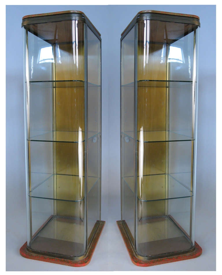 a very special pair of 1930's tall slender showcases, having beautifully patinated brass cases, and curved glass fronts. mounted on painted wood bases, with hinged brass doors on the back. excellent condition with all the original glass including