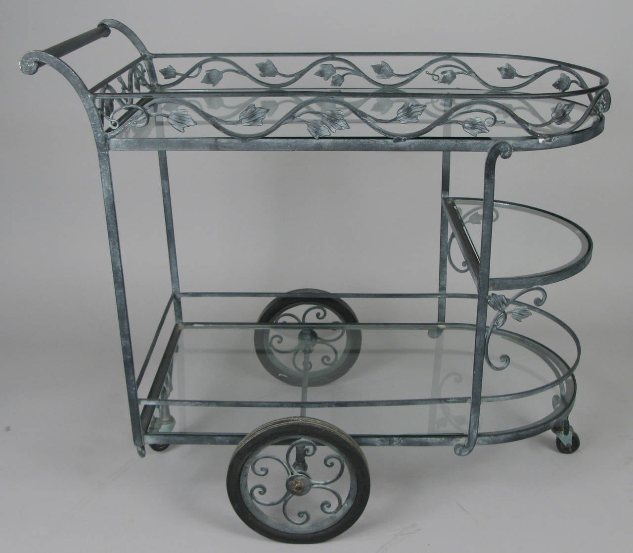 A beautiful vintage 1940s wrought iron rolling bar cart by Salterini. Very well made with a nice patina on the iron. Full size glass shelves above and below and a small glass shelf halfway up as well.