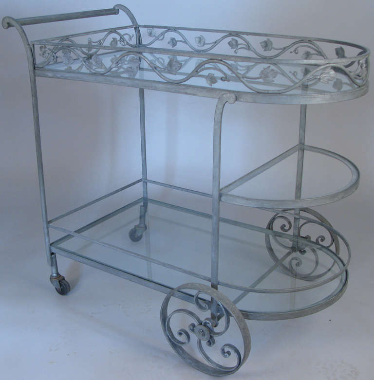 a very charming and extremely functional wrought iron rolling bar cart by Woodard c. 1950. beautiful design with curved front and scrolled handle. two full glass shelves and one smaller curved glass shelf as well.