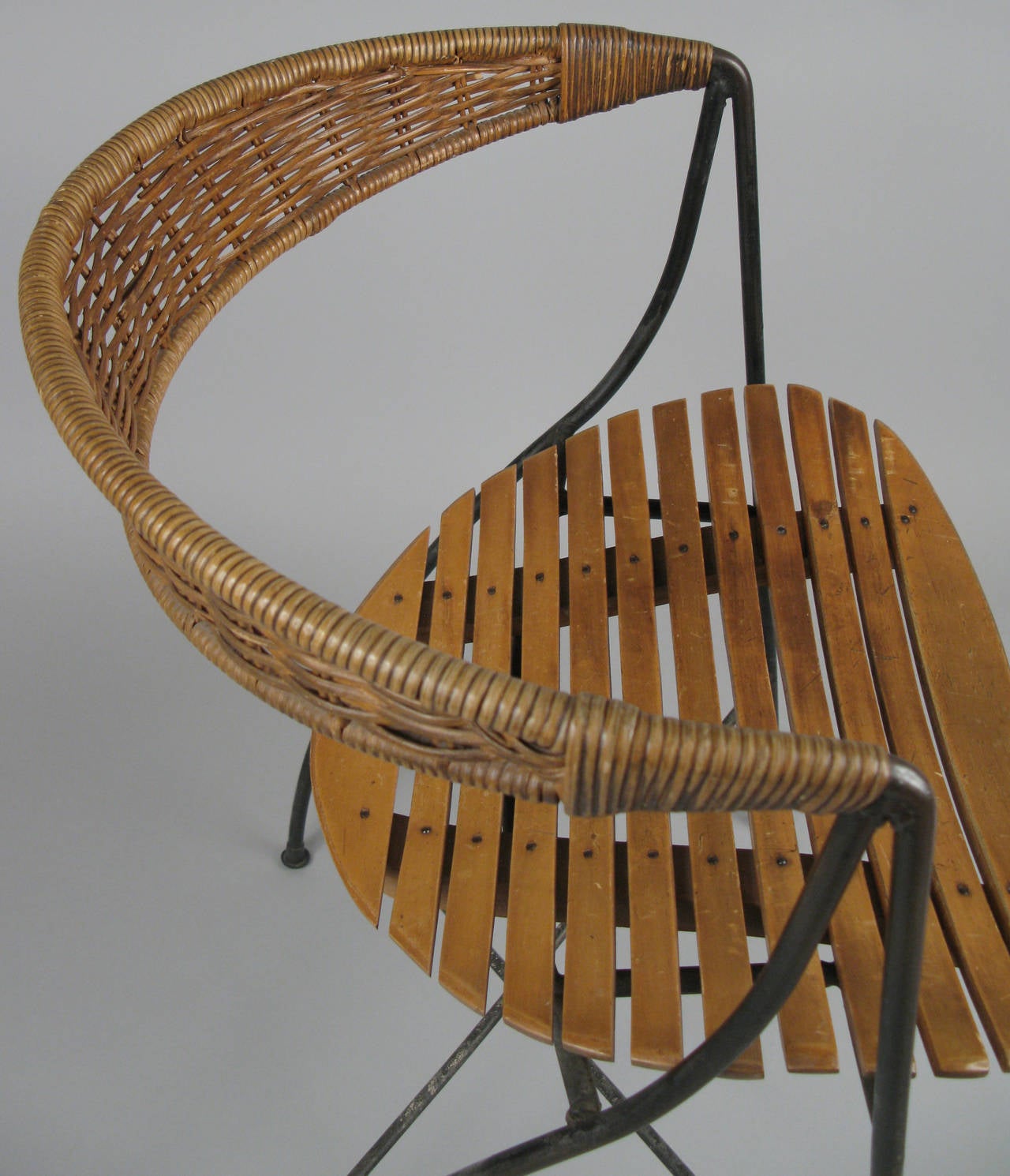 A rare example of Arthur Umanoff beautiful 1950s cane back iron chair. One of his most engaging designs with a sculptural wrought iron frame, curved slat maple seat, and curved and tapered wicker caned back. Original condition with two repairs to
