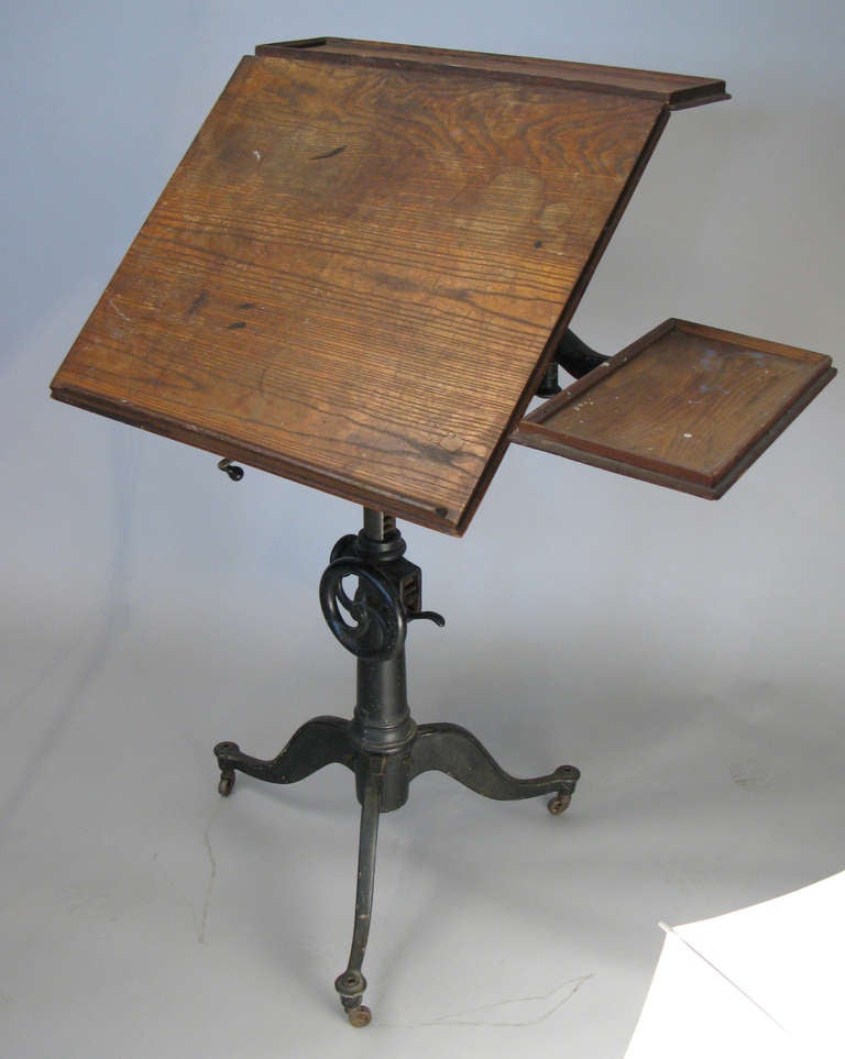 a very handsome antique adjustable tilt-top drafting table c. 1910 with a cast iron base, cast iron height adjustment wheel, and tilt mechanism for the top, which also connects to the top ledge which stays horizontal regardless of the tilt angle of