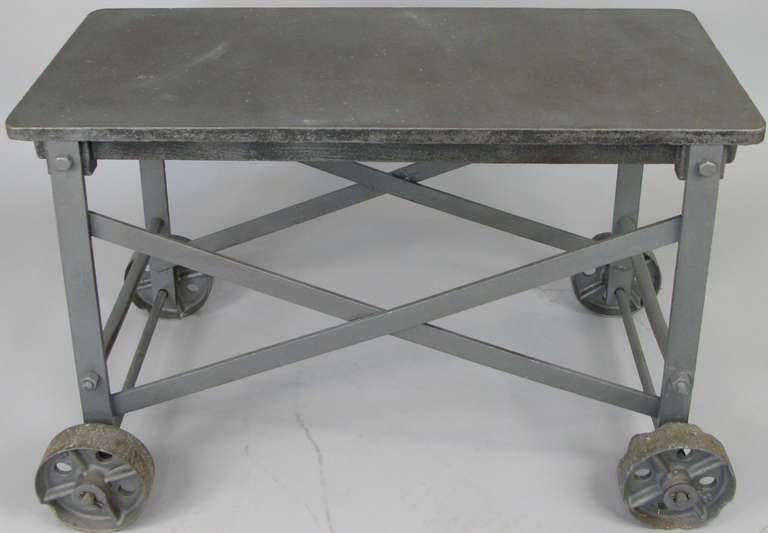 a very unique antique industrial table with cast iron top and steel base mounted on cast iron wheels. originally used in a glass blowing factory in the early 20th century.