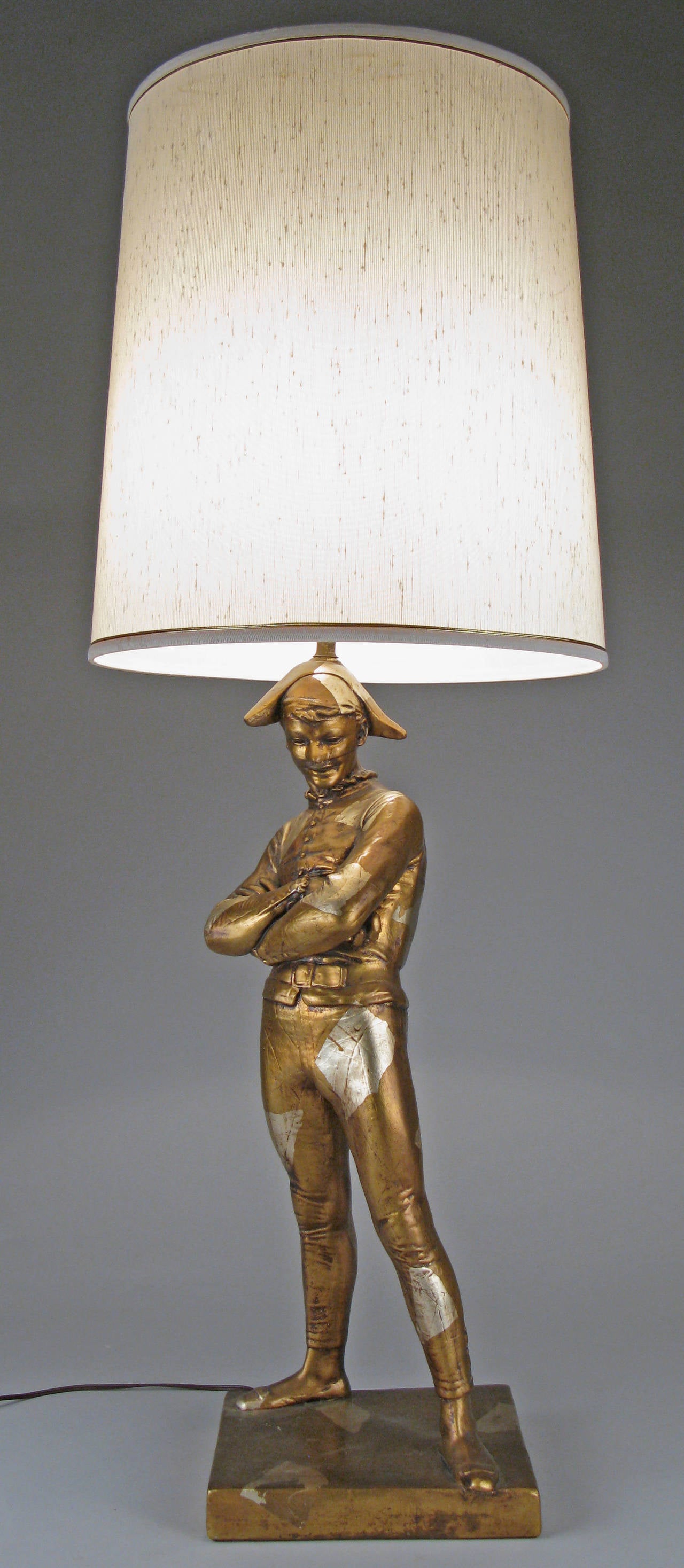 A very charming and well made 1960s plaster lamp in the form of a court jester finished in a harlequin pattern in gold and silver leaf. Classic form in very good condition.

Height of the jester is 27