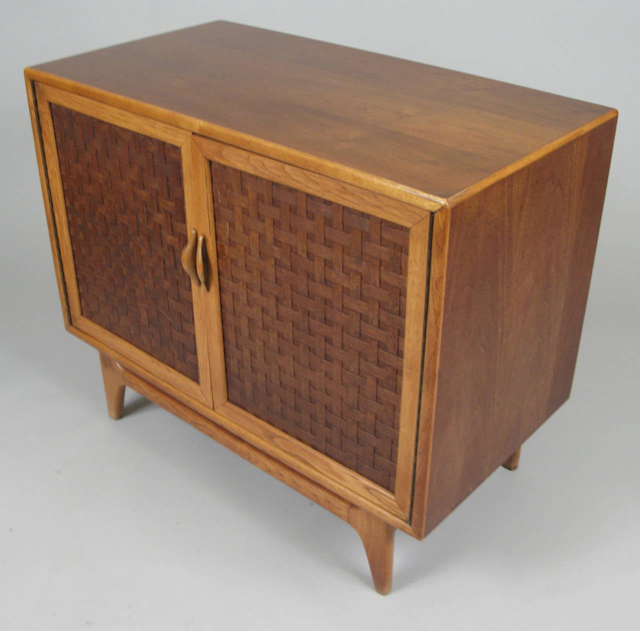 A very handsome 1960s two-door cabinet in oak with beautiful woven patterned panels inset into the doors. Interior has a single adjustable shelf.