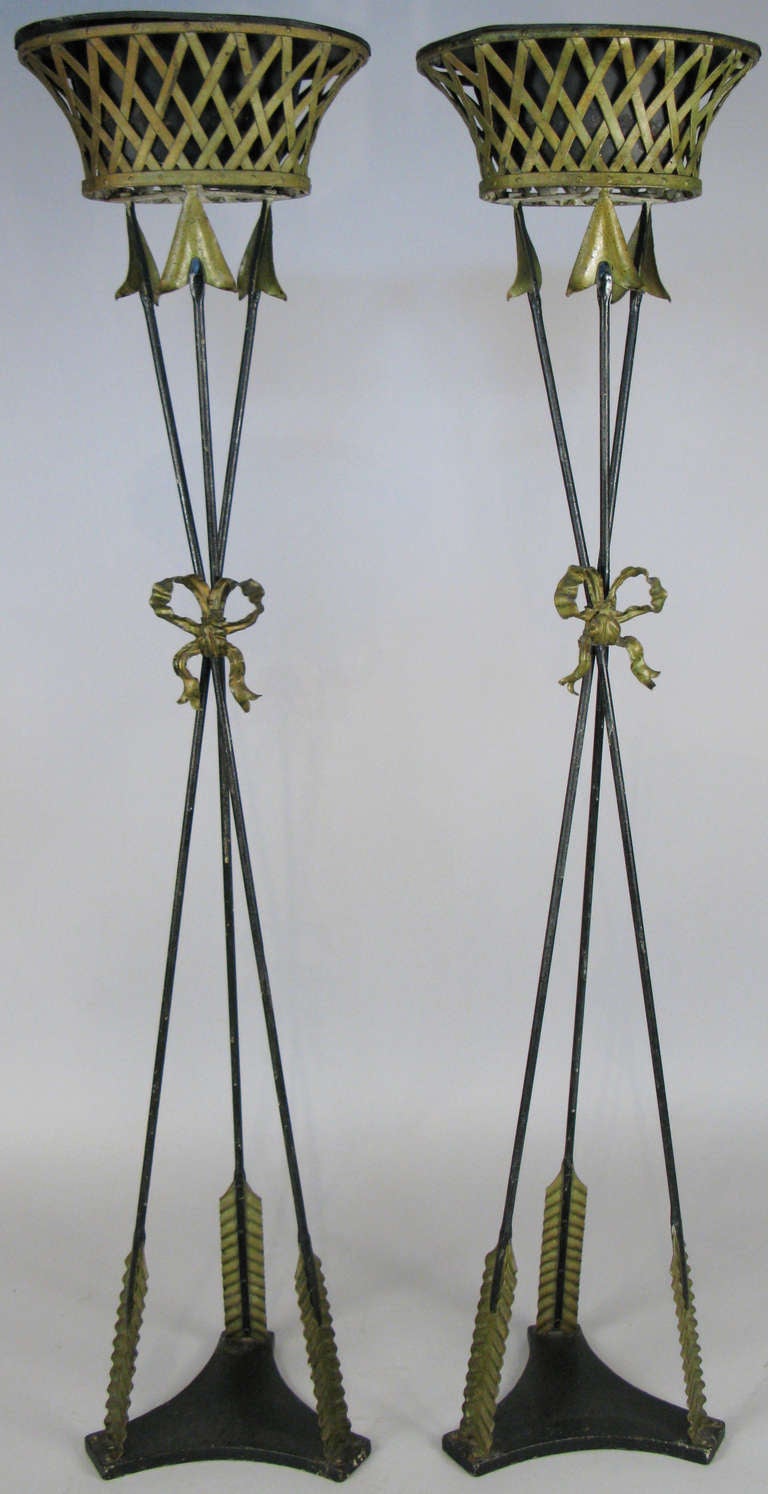 a charming pair of 1920's iron neoclassical tall plant stands, with three arrows gathered by an iron bow, supporting a flared oval lattice bowl. mounted on heavy iron bases. 