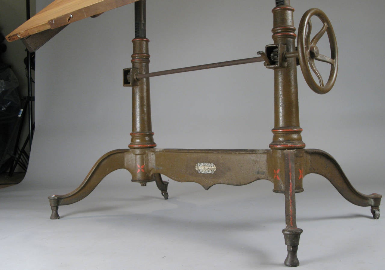 a very handsome antique 1920's fully adjustable drafting table by Dietzgen, with a cast iron base with wheel adjustment for height and a separate one for the tilt mechanism. the table can be placed securely at any angle including completely flat.