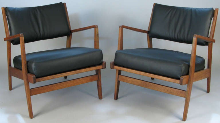 a pair of classic modern 1950's lounges chairs by Jens Risom with walnut frames and black leather upholstery. one of Risom's best lounge chair designs, with angled frames and curved backs.