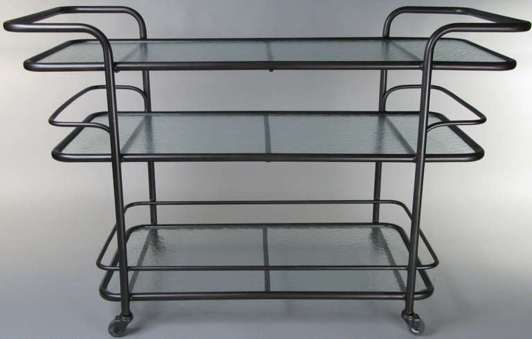 A very nice vintage 1950s rolling bar cart with tubular aluminum frame in the style of Walter Lamb. Great design with integrated handles and 3 glass shelves, the lowest one with a full safety rim. finished in dark bronze.