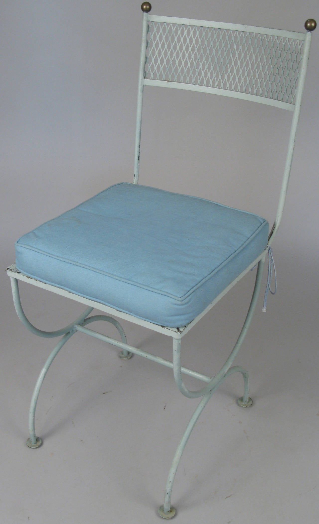 A very charming set of eight 1950s iron garden chairs with brass ball finials, having curved backs and Curule bases. All in their original powder blue finish, with seat cushions in original fabric, which will need reupholstery.