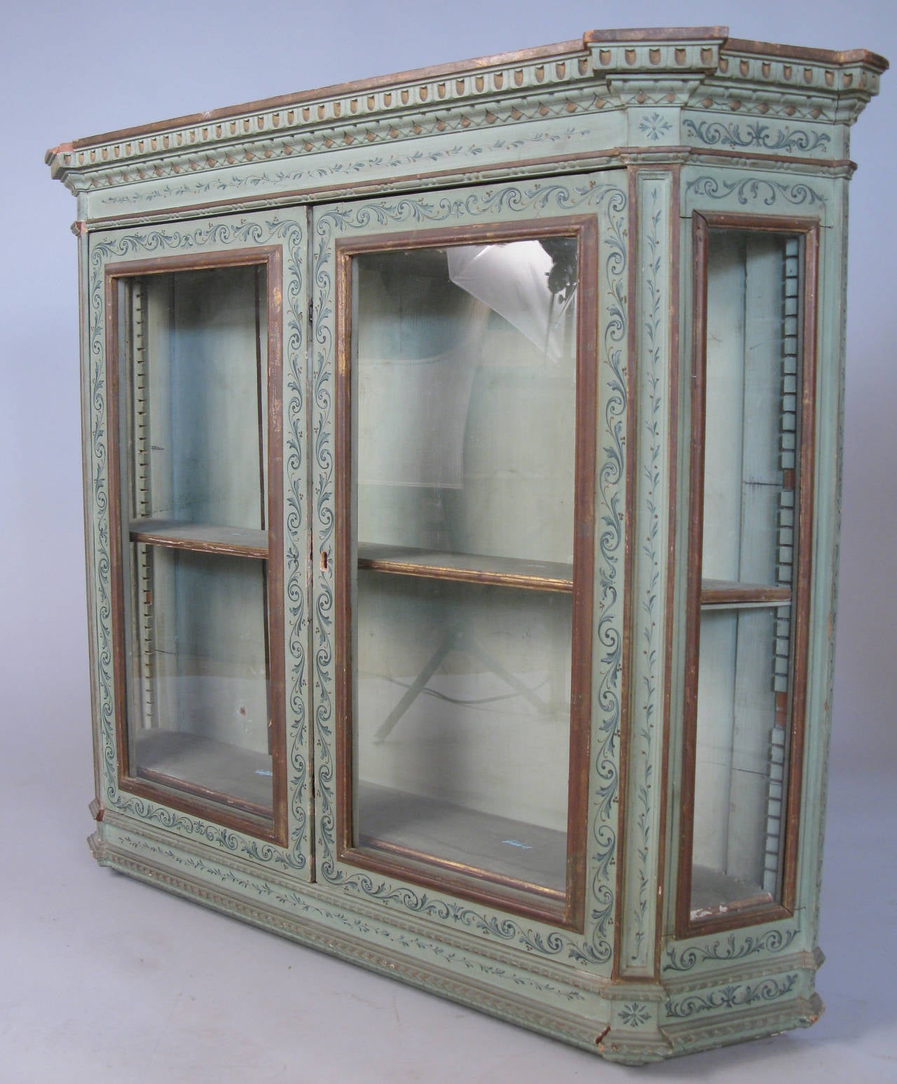 A charming Italian wall-mounted display cabinet, in its original pale green finish with hand-painted details all-over. Beautiful design with a pair of hinged glass doors, and adjustable shelves, with canted glass side panels as well.