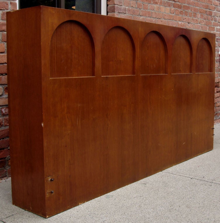 a walnut storage headboard with arcade detail concealing storage across the top, and a drop-down table in the center.