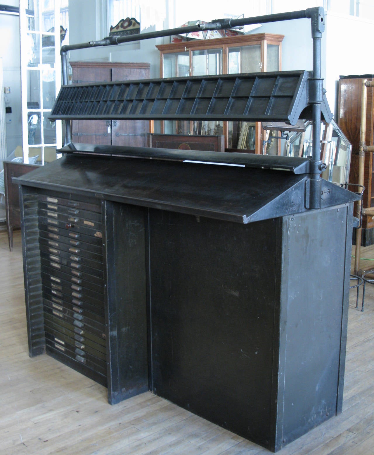 an antique steel double-sided typesetters work station with a bank of divided drawers on each side to store type, and several tiers of angled work surfaces above used for handling and setting printers type.