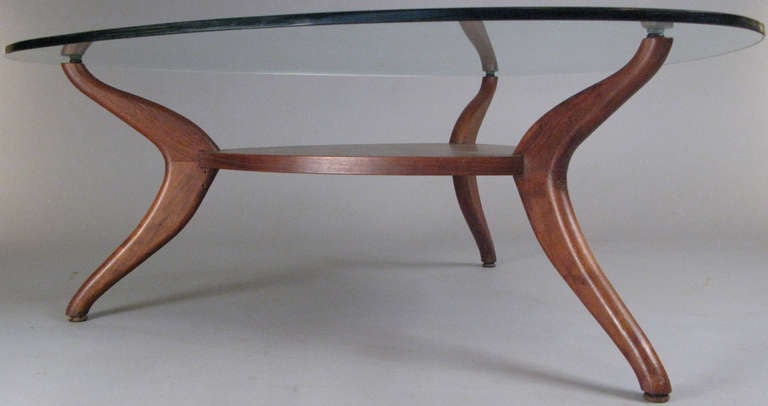 a dynamic 1960's modern cocktail table with a sculptural base of polished walnut connected to a low shelf, and with a triangular glass top. In the style of Vladimir Kagan.