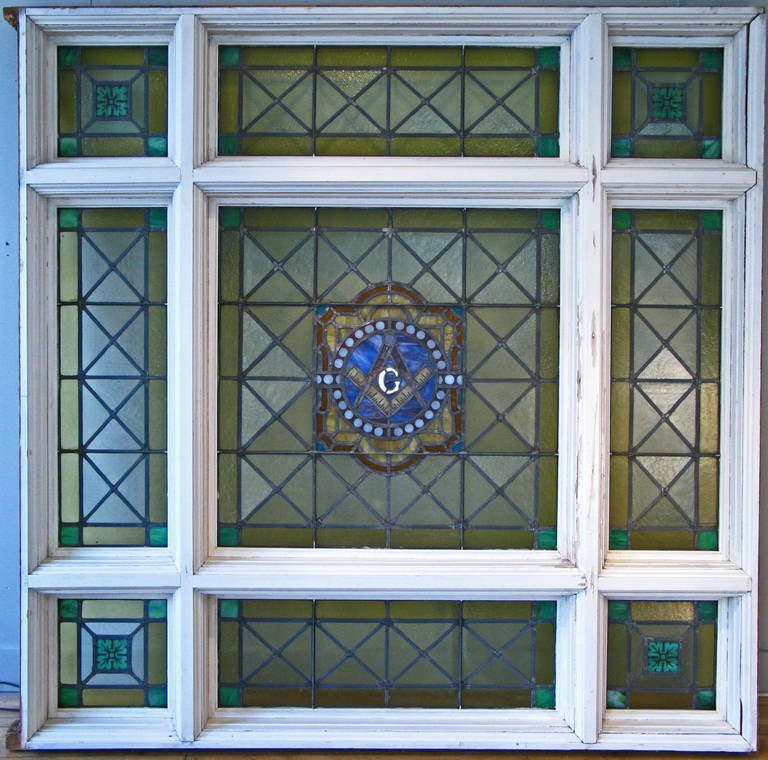 A monumental stepped wood frame divided nine pane architectural stained glass window from a Masonic Lodge in western NY state. All in opaque glass, border panes and gold and teal, with center medallion with masonic icons. Very good condition with