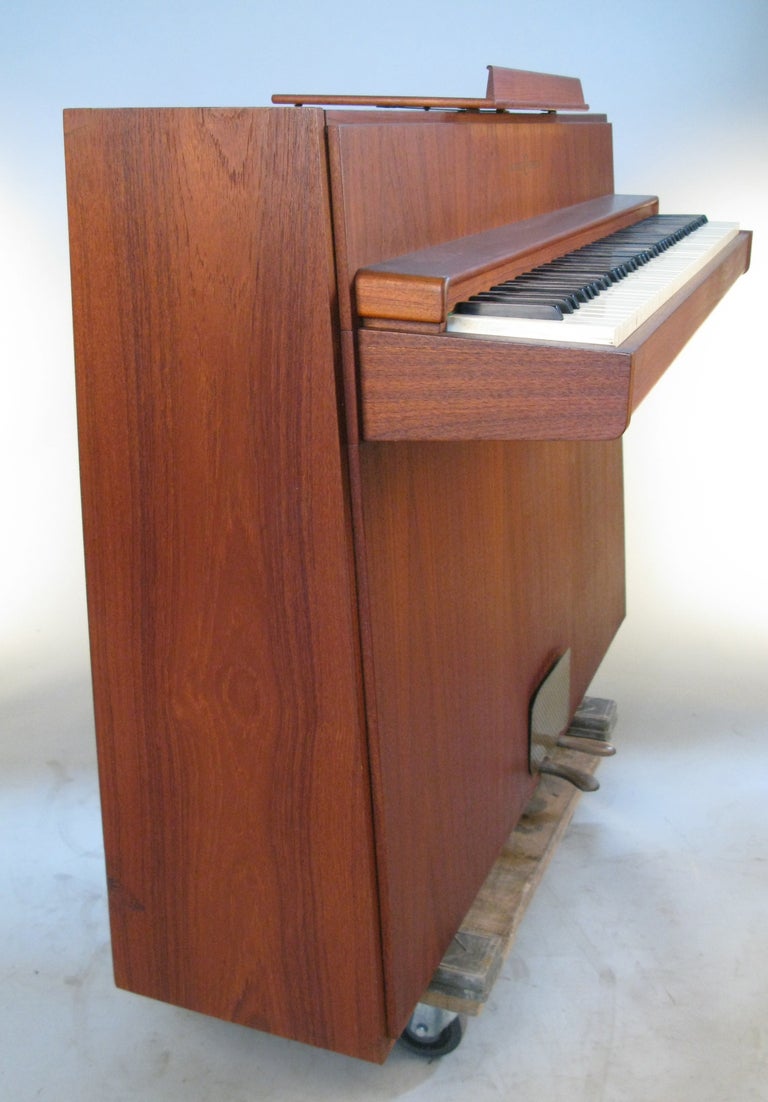 a beautifully made upright piano with a gorgeous teak case made by Andreas Christensen c. 1960. classic danish design with a spare case and keyboard, with folding music stand.