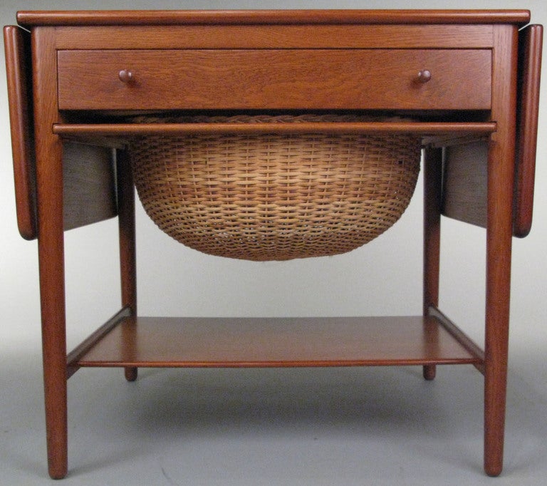 Hans Wegner's classic 1950's sewing table/cabinet in beautifully grained teak. a very nice design with drop leafs on both sides for a variety of work surface areas. this table has the original basket which sits in the slide out tray. the single