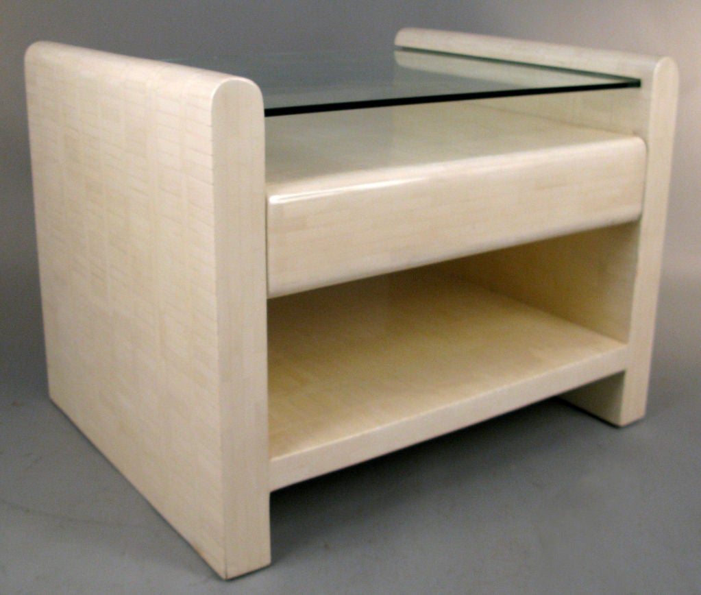 a large form lamp table or nightstand with a surface of tasselated bone mosaic tile, all in neutral ivory, with a glass top, a single drawer, and a lower shelf. great form and a very substantial table.