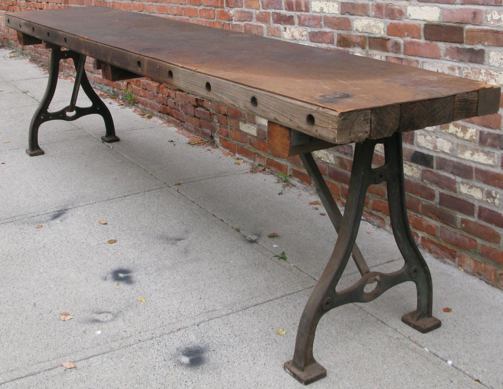 an unusual very long antique table with heavy cast iron bases at each end. top made from utility pole crosses, with a masonite surface. great size and proportions.
