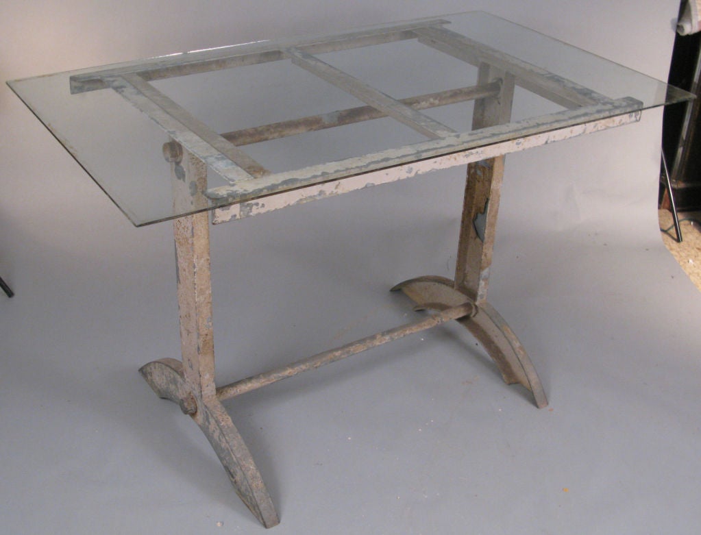 a very unique antique industrial cast iron table, having a trestle base with demi-lune feet, supporting a grid top, perfect for the included glass top, or would be nice with an antique wood top as well. base is in its original worn gray painted