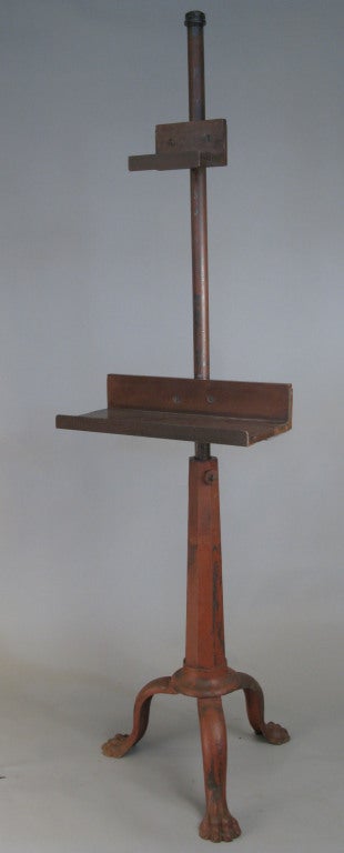 a fantastic large and very heavy cast iron base industrial easel stand, having a 3 leg base with paw feet, supporting a faceted and tapered cast iron stand and adjustable pole. mounted on the pole are an adjustable cast iron and wood base and top