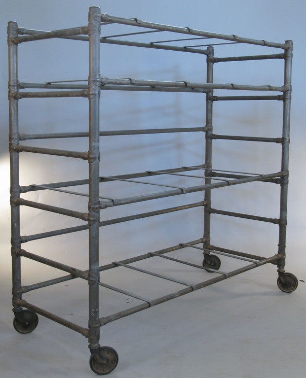 an outstanding large antique industrial cast iron rolling cart with 4 shelves and beautiful details. raised on its original large slim wheels, with adjustable mounts for the crossbars. the shelves rest on moveable cast iron supports. comes with 4