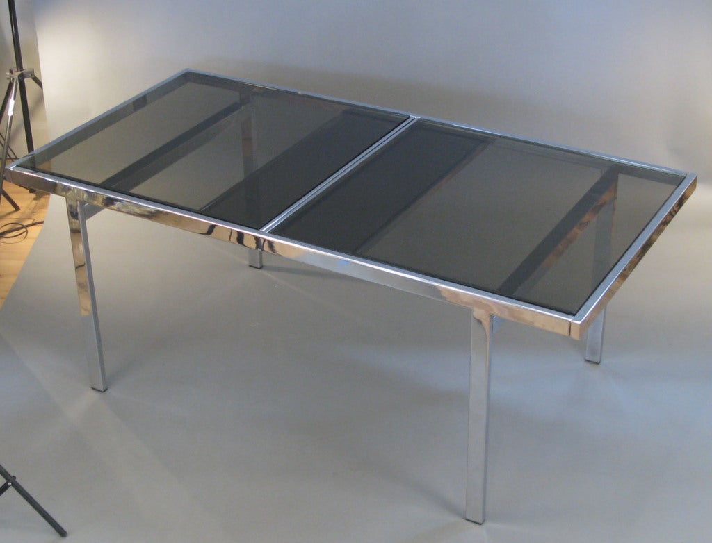a very nice c. 1960's extension dining table with a chromed steel frame and smoked glass panel top. the top is in 2 sections which slide apart to allow the recessed leaf to be raised up, increasing the top to 95
