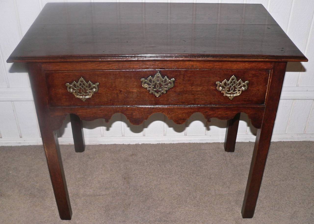 This Geo. III side table has chamfered legs, a moulded edge and a shaped apron on three sides. Super deep oak color with great patina to the wood. The pierced brass plates are original to the table. Very clean top with a few faded ink marks as seen