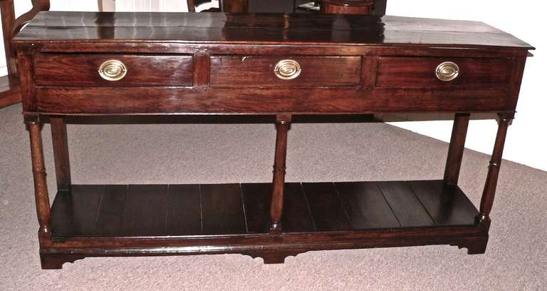 This oak pot board dresser base originates from Camarthen region of South Wales and has a very good color and patina. It is quiet narrow in depth at 17'' and stands high. It has three drawers across with turned leg supports. A very pretty and well