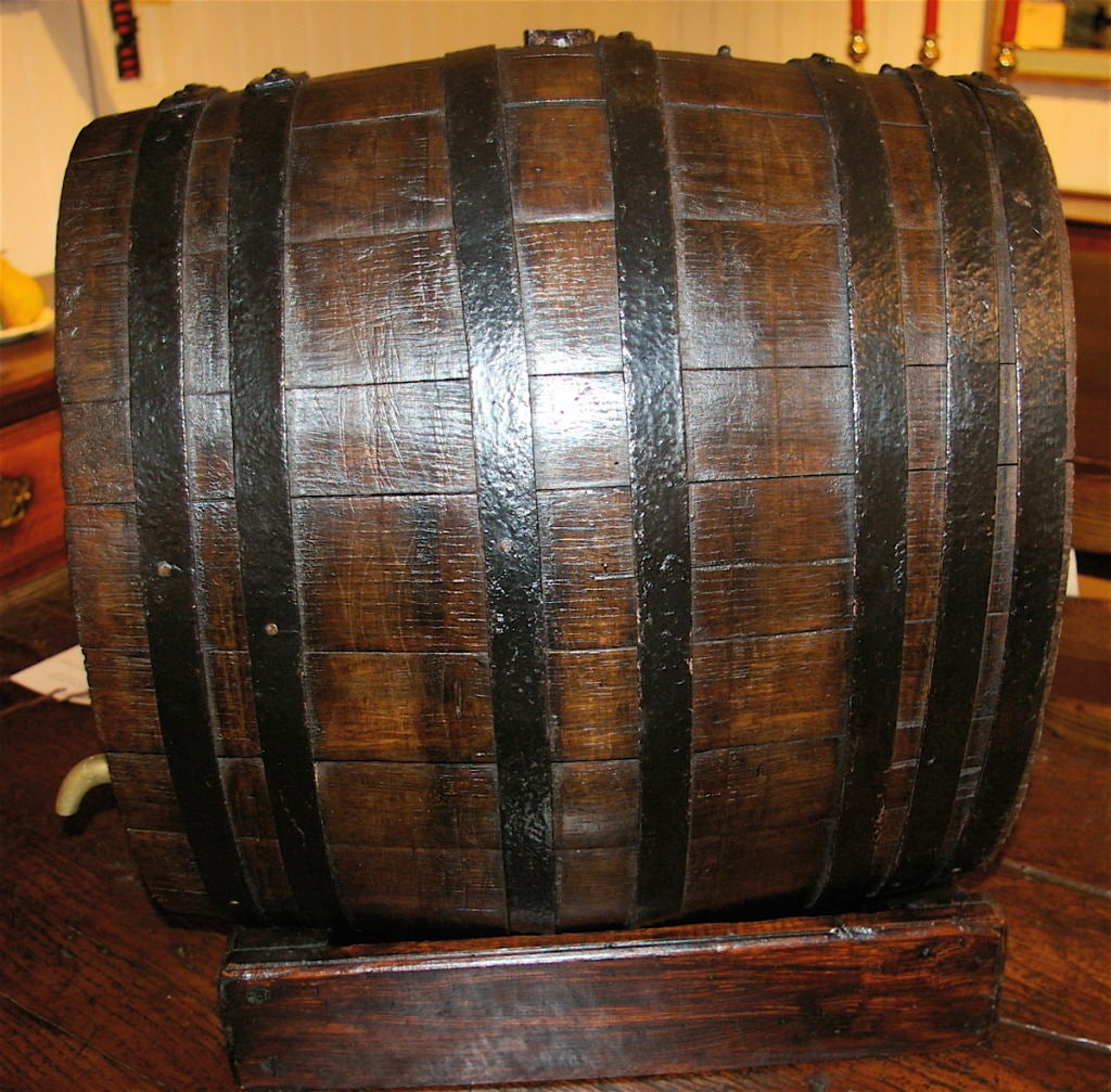 This wine barrel is a smaller version that can be displayed on a table and is coopered with iron bands. It has a brass spigot and sits on a later wood stand. Originating from Burgundy, it might have come from a brasserie or cafe.