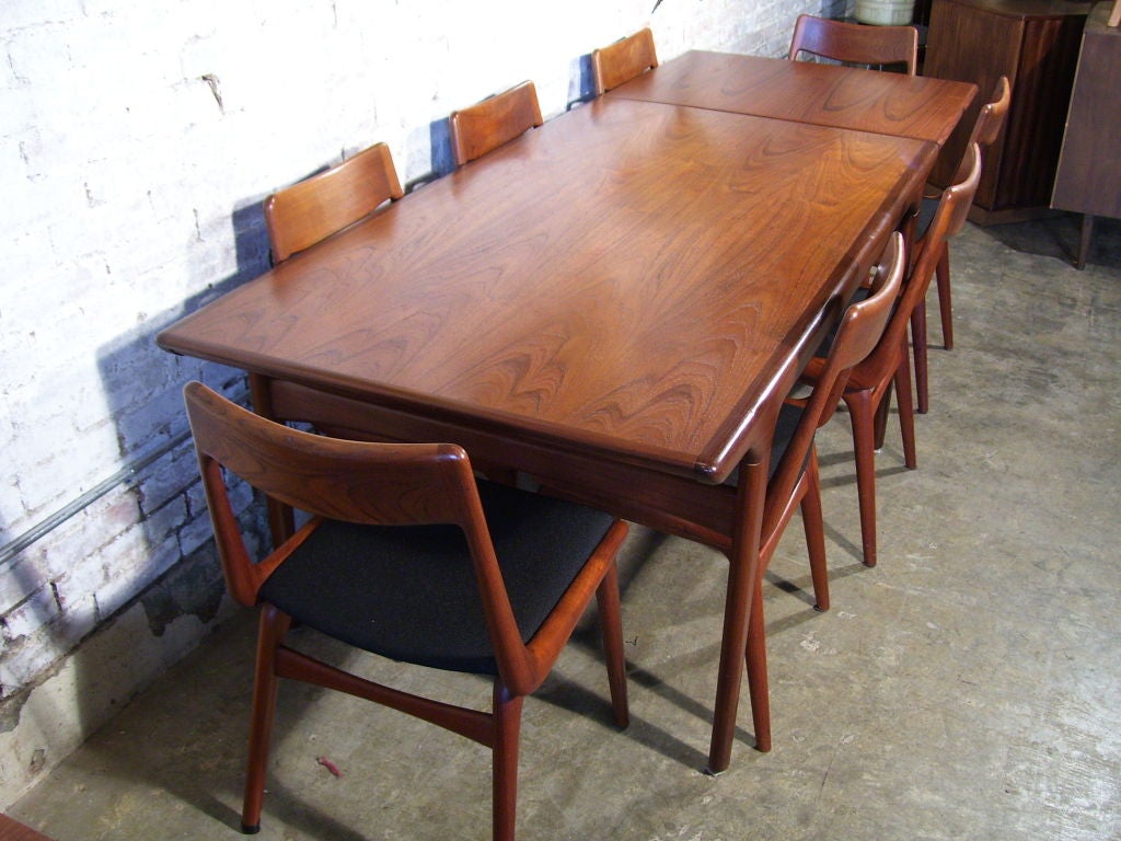 Beautiful teak draw leaf dining table with eight dining chairs covered in black hopsack material. The table is 95