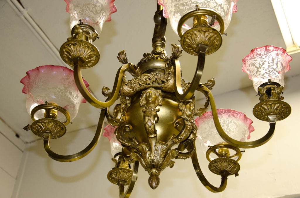 This fabulous American Victorian chandelier has all the elements of a top of the line fixture.  Beautiful two-toned patina in gold and brown heightens the quality metal work.  The shades are period to the light and are stencil-etched with cranberry