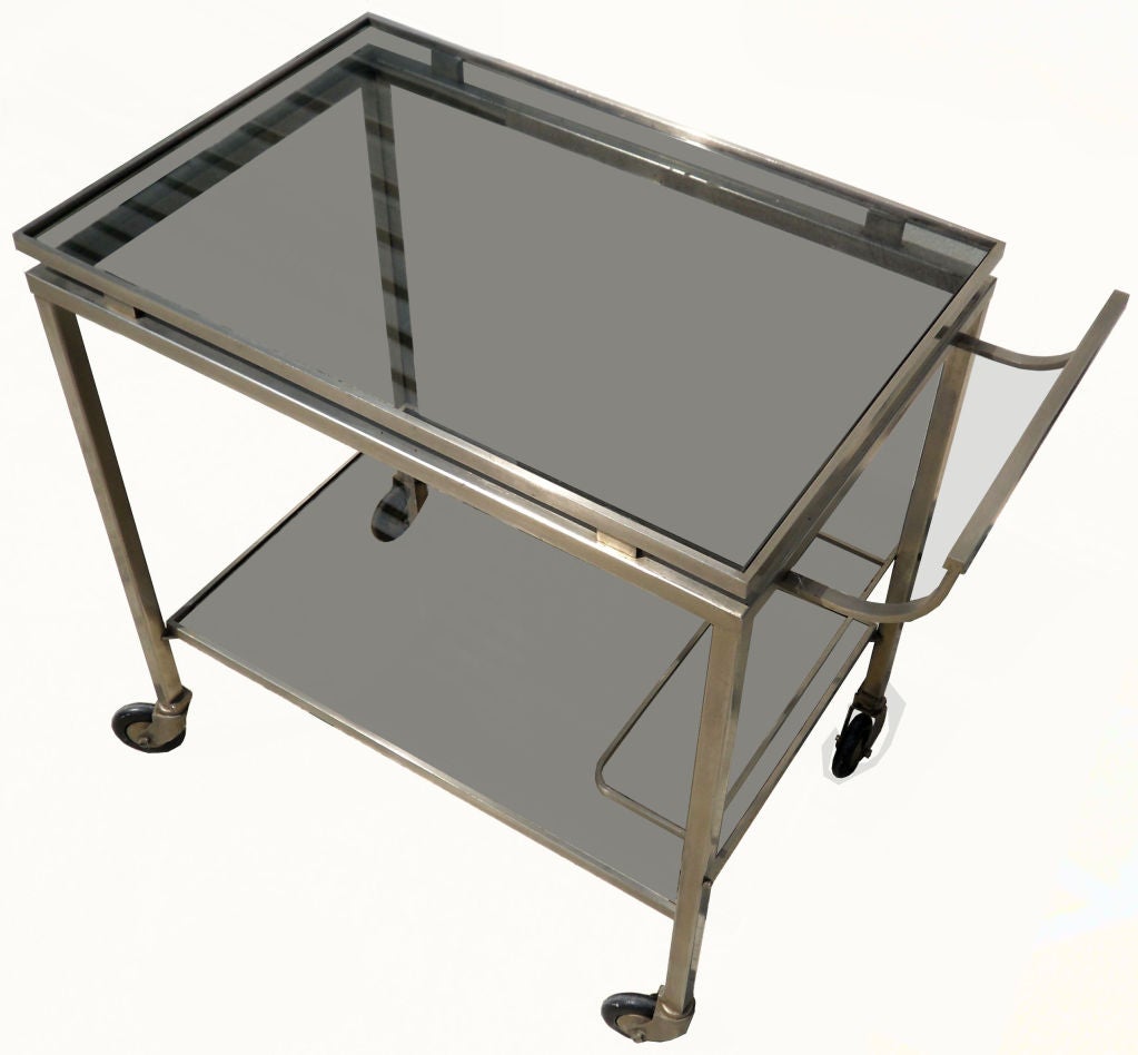1 of 2 bar cart two-tier by Guy Lefevre for Maison Jansen. 
1960 in Chrome with smoked Glass Shelves and all original wheels.
24 inches Length without the handle, 29 inches L overall, 27.5 inches H overall, 25.3/4 inches H without the handle, 8