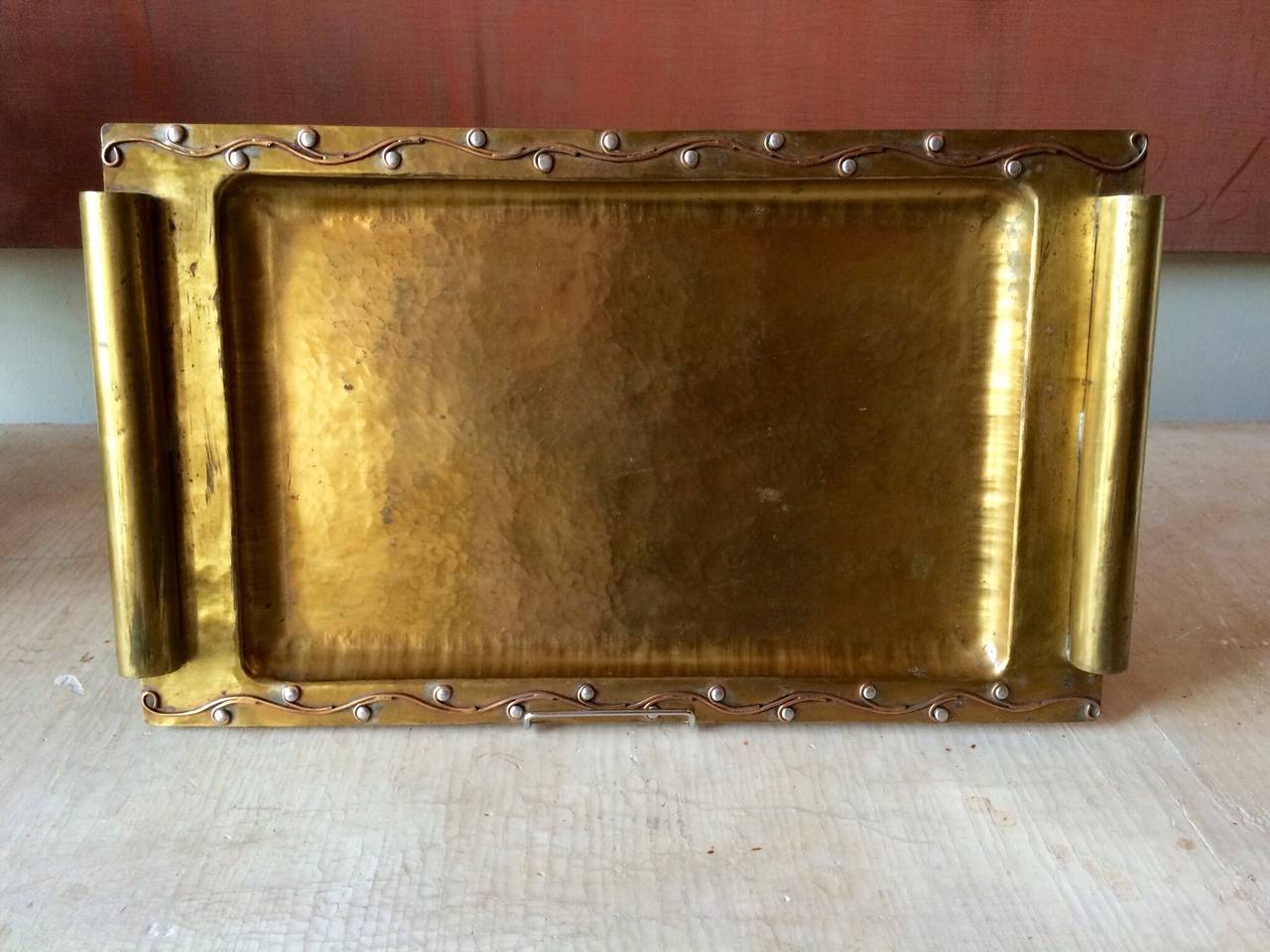A handcrafted hammered rectangular brass handled tray with copper and silver raised trailing vine design.
